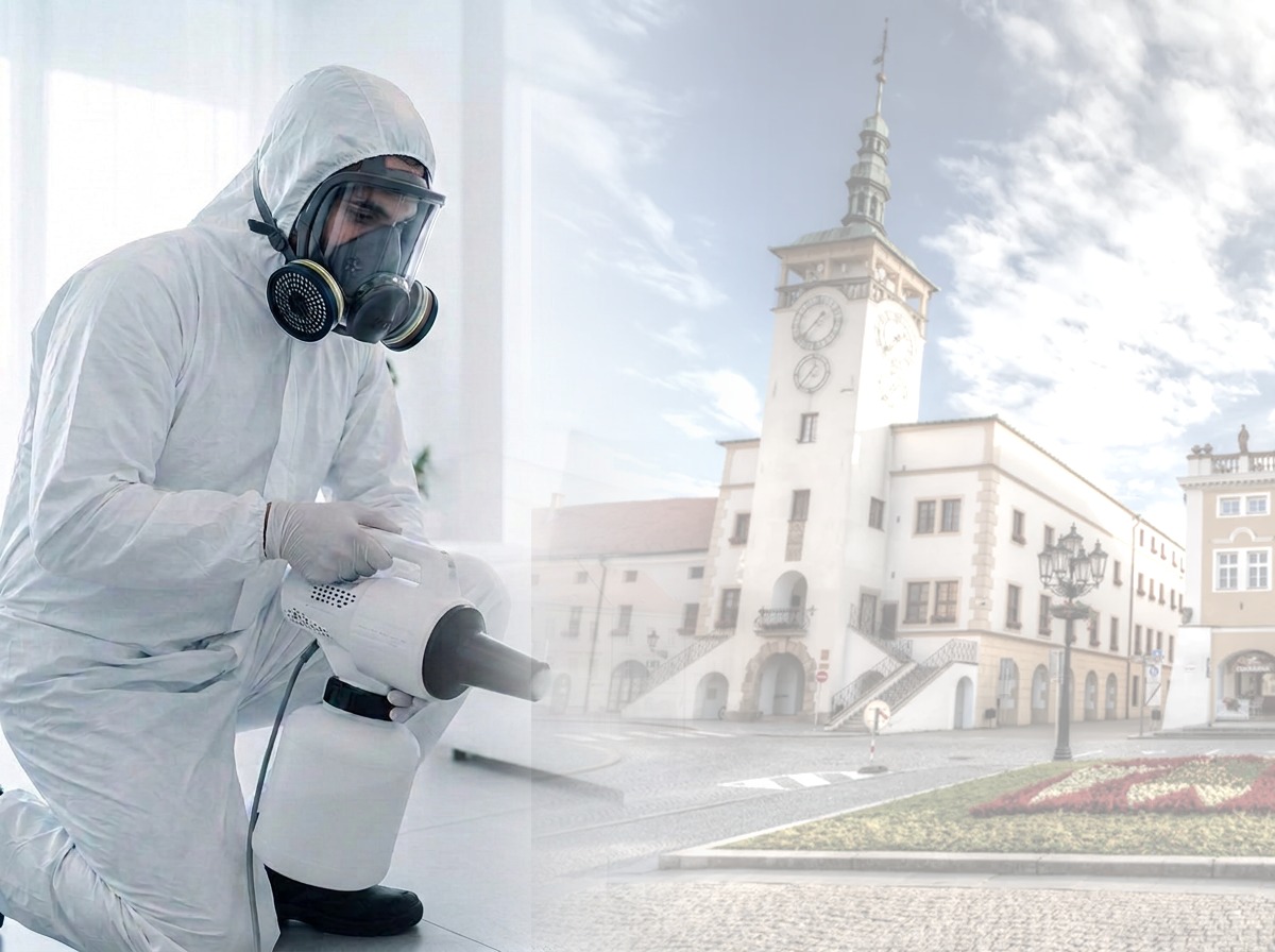 Technik v ochranném obleku s celoobličejovou maskou aplikuje ULV dezinfekci, v pozadí radnice v Kroměříži